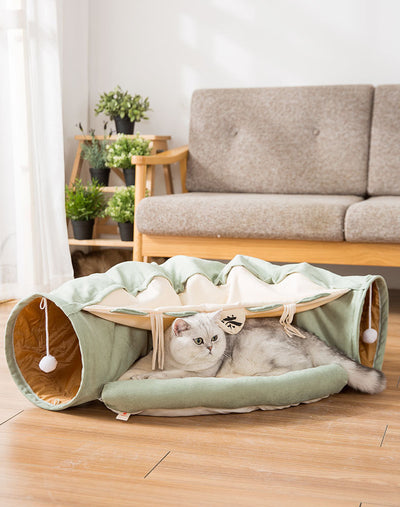 Cat lying on a green pet bed with tunnel in a living room setting